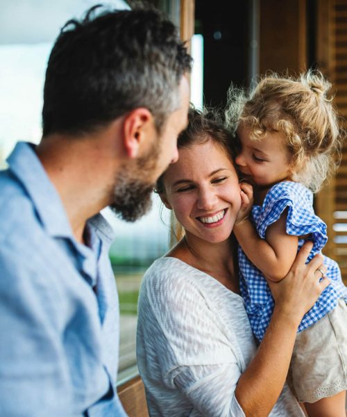 Family,With,Small,Daughter,Sitting,On,Patio,Of,Wooden,Cabin,